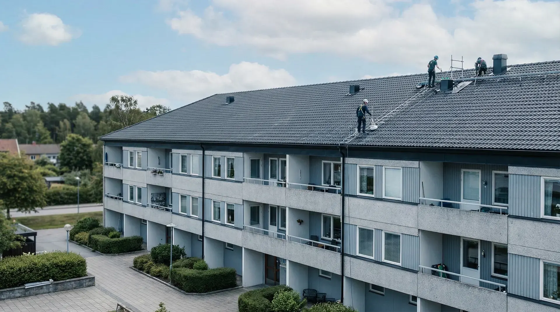 Takarbetare på flervåningshus med grå fasad och tegeltak.