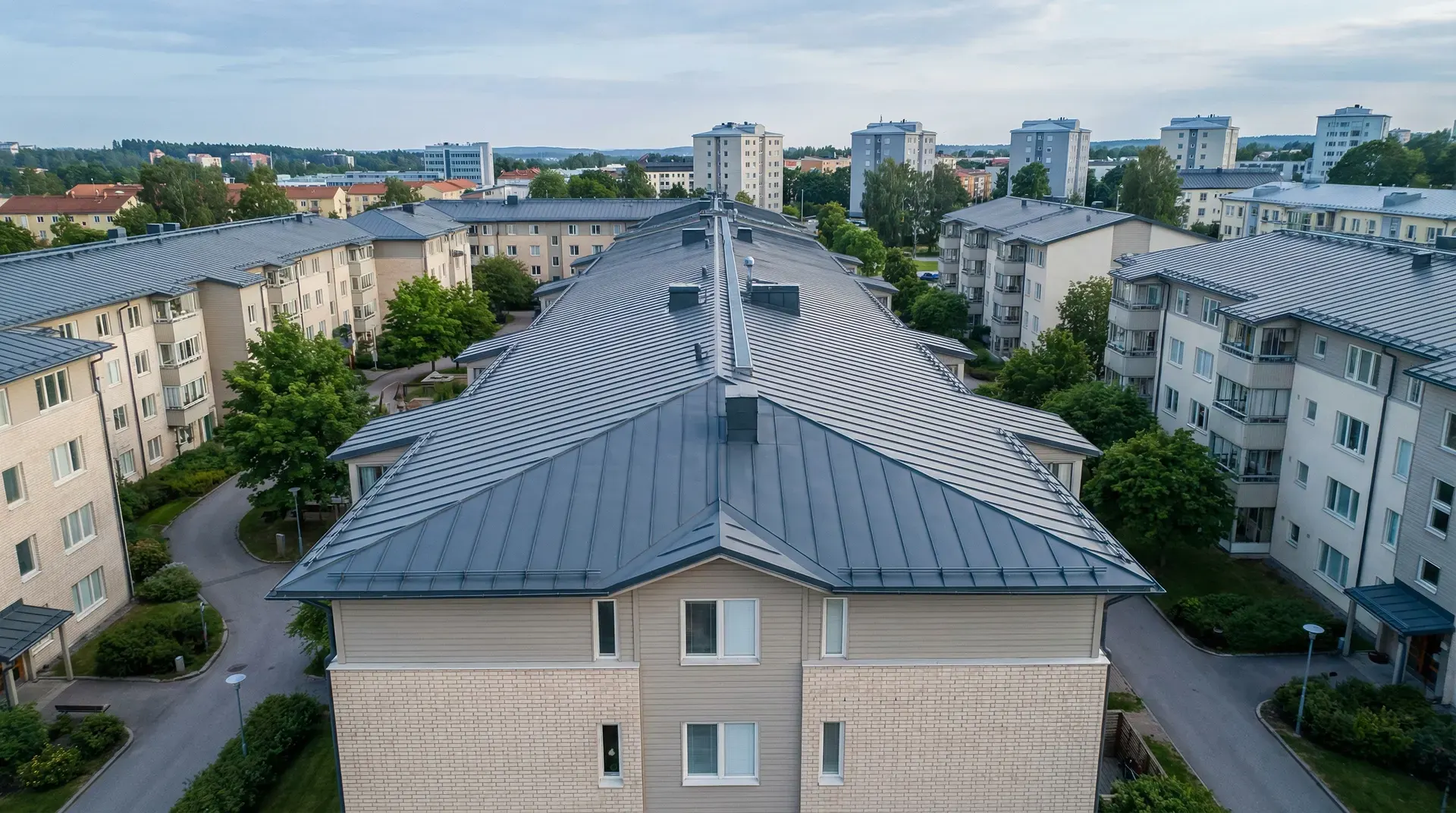 Flygfoto av flerbostadshus med grå plåttak i bostadsområde.