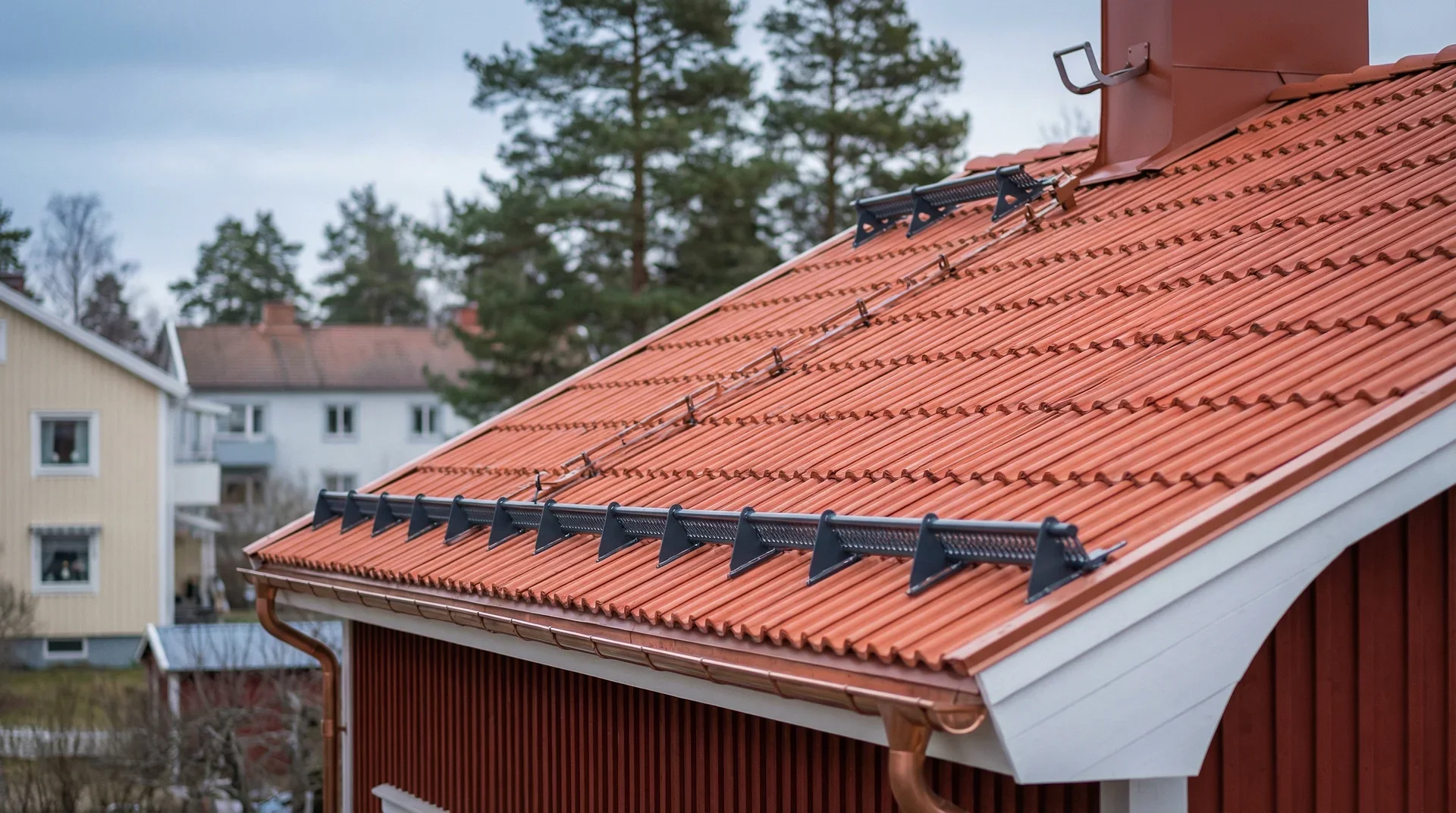 Rött tegeltak med snörasskydd och kopparränna i bostadsområde.