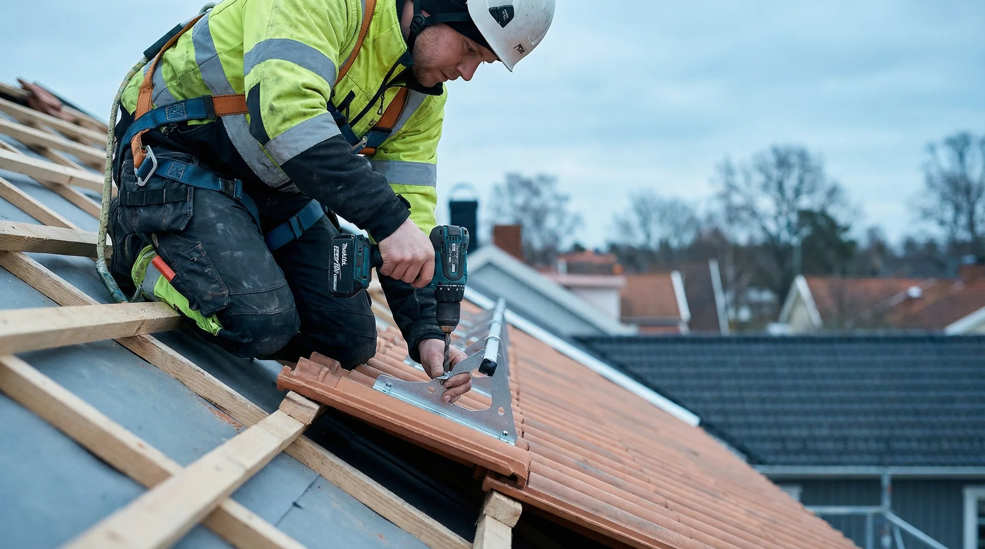 Takläggare i skyddsutrustning fäster takpannor med borrmaskin på tak.